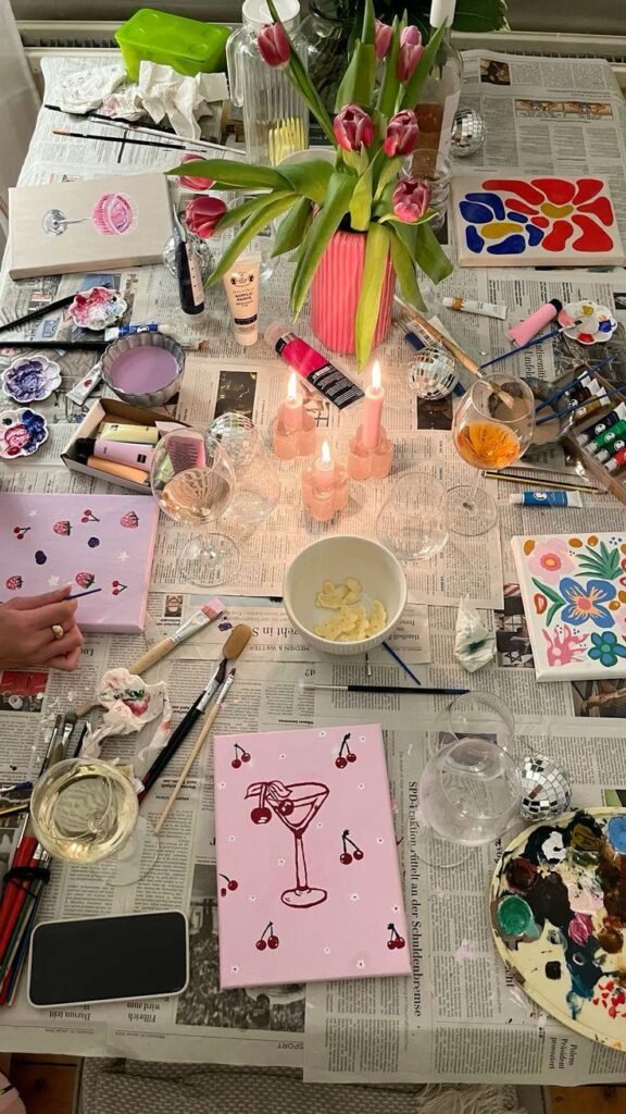 A table with DIY things, paintings, painting supplies, candles, flowers, mugs, an event for girls.