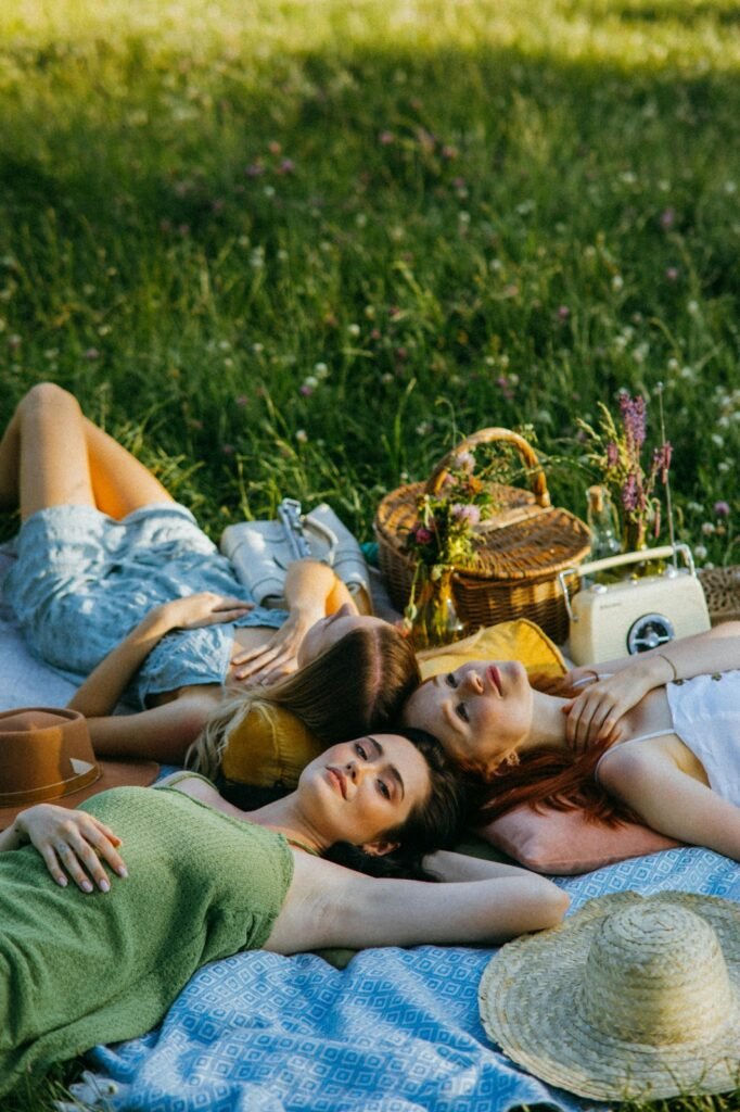 A group of girls, sitting in the grass, on a meadow, having a picnic and relaxing